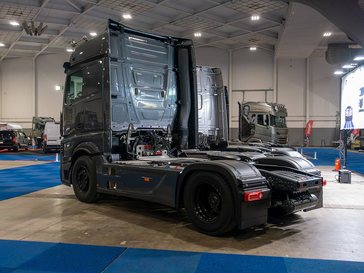 Tmavě šedý tahač Mercedes-Benz Actros L bez návěsu ve výstavní hale, pohled zezadu z levého boku