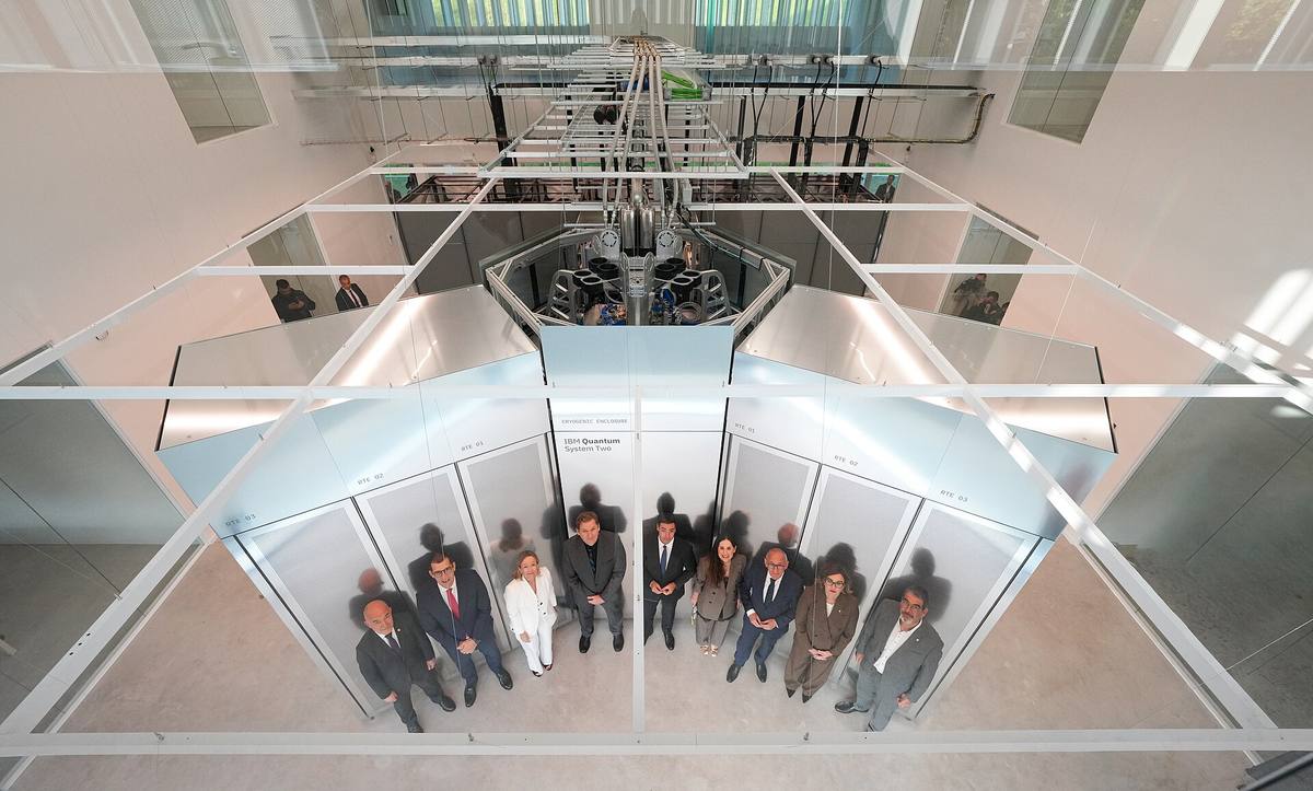 Kvantový počítač IBM Quantum System Two ve skleněné hale, pod ním stojí skupina lidí
